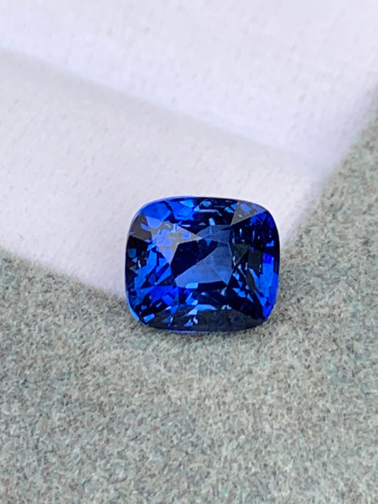 Gros plan d'un Saphir bleu • 3,02ct de [NOUVEAU] Bonnot Paris repose sur une surface beige douce sur un fond rose clair, ses facettes scintillant de nuances de bleu.
