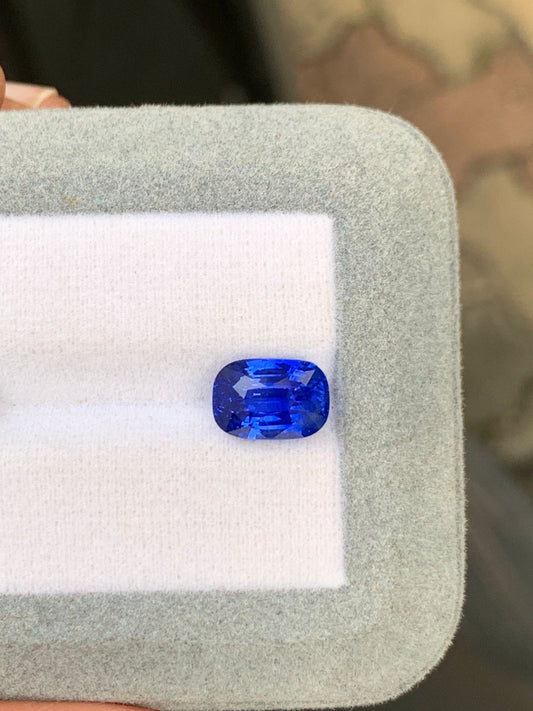 Un saphir bleu du Sri Lanka de 4,60 carats signé Bonnot Paris repose sur un coussin moelleux blanc et gris. Cette pierre rectangulaire aux bords arrondis brille de sa couleur profonde et de ses facettes réfléchissantes, témoignant de son attrait de pierre précieuse prisée.