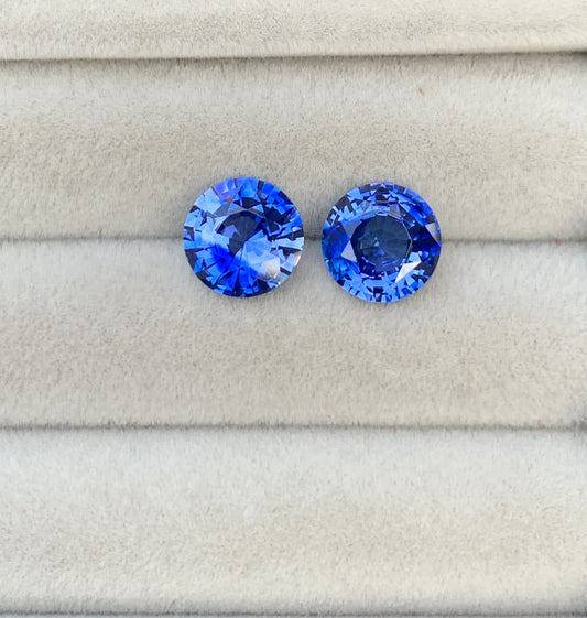 Deux pierres précieuses saphir bleu de 4,90 carats de [NOUVEAU] Bonnot Paris reposent sur un tissu gris clair, mettant en valeur leur couleur vibrante et leurs facettes complexes, incarnant l'attrait des pierres précieuses haut de gamme.