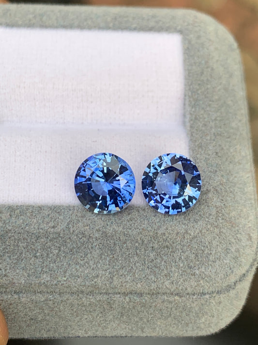 Deux pierres bleues rondes de Bonnot Paris, totalisant 5,65 carats, reposent sur une surface grise douce et coussinée. Ces saphirs bleus sont savamment facettés pour sublimer leur éclat sur un fond blanc, dans un sertissage gris.