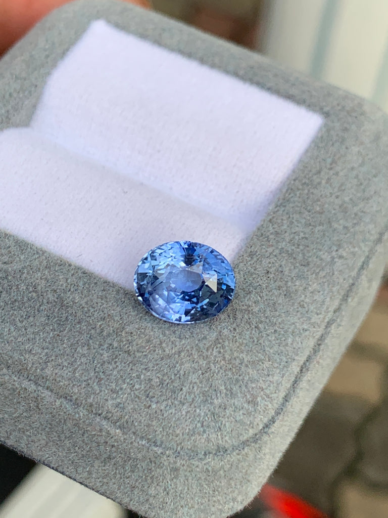 Gros plan sur la pierre précieuse Saphir bleu • 4,02ct de Bonnot Paris, scintillante dans un écrin gris à l'intérieur blanc, sur un fond légèrement flou.