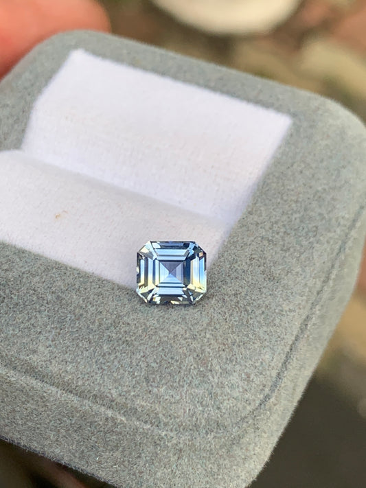 Le Saphir bleu pastel de 2,10 carats de Bonnot Paris, provenant du Sri Lanka, brille avec élégance sur un doux coussin blanc, dans un écrin de velours gris. Son éclat est sublimé par le flou du fond, soulignant sa beauté éblouissante parmi d'autres pierres précieuses.