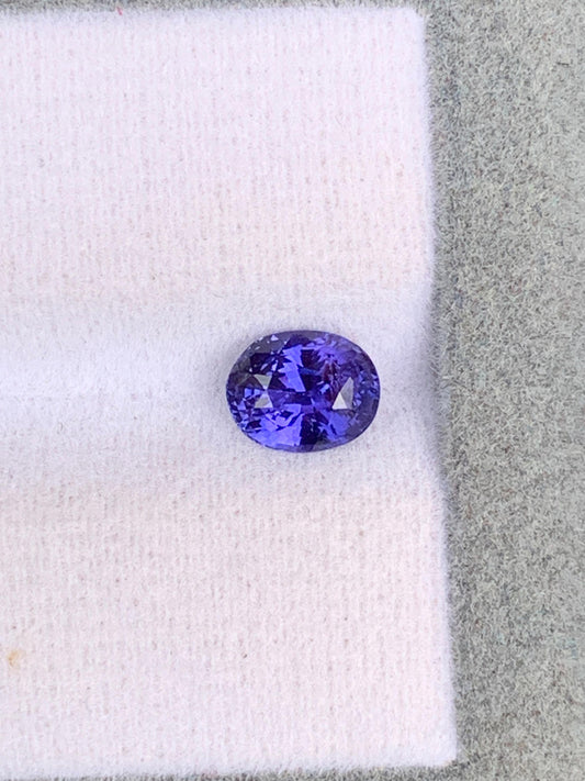Le Saphir violet • 1,10ct de [NOUVEAU] Bonnot Paris, une exquise gemme ovale du Sri Lanka, repose sur une surface texturée grise et blanche, reflétant la lumière pour révéler ses facettes étonnantes et son allure intemporelle.