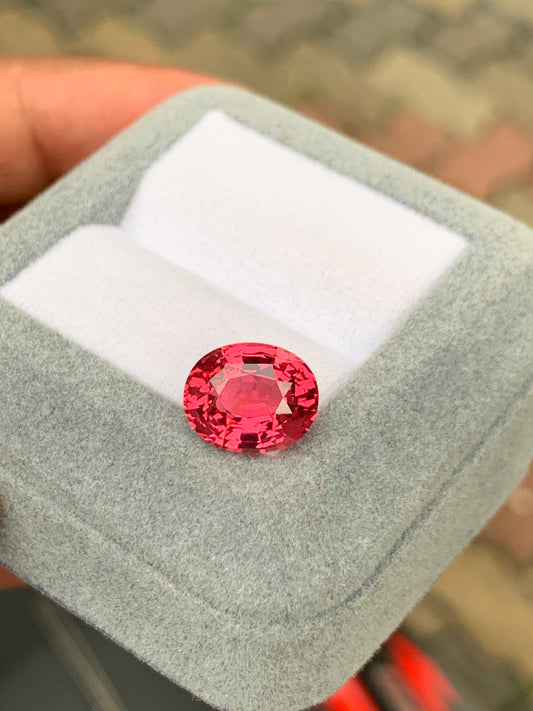 Une pierre précieuse Spinelle Mahenge de 5,00 carats de la marque Bonnot Paris [NOUVEAU] scintille dans un petit écrin gris clair doublé de tissu blanc. Tenu à la main, il se détache sur un arrière-plan flou, révélant le charme de la haute joaillerie.