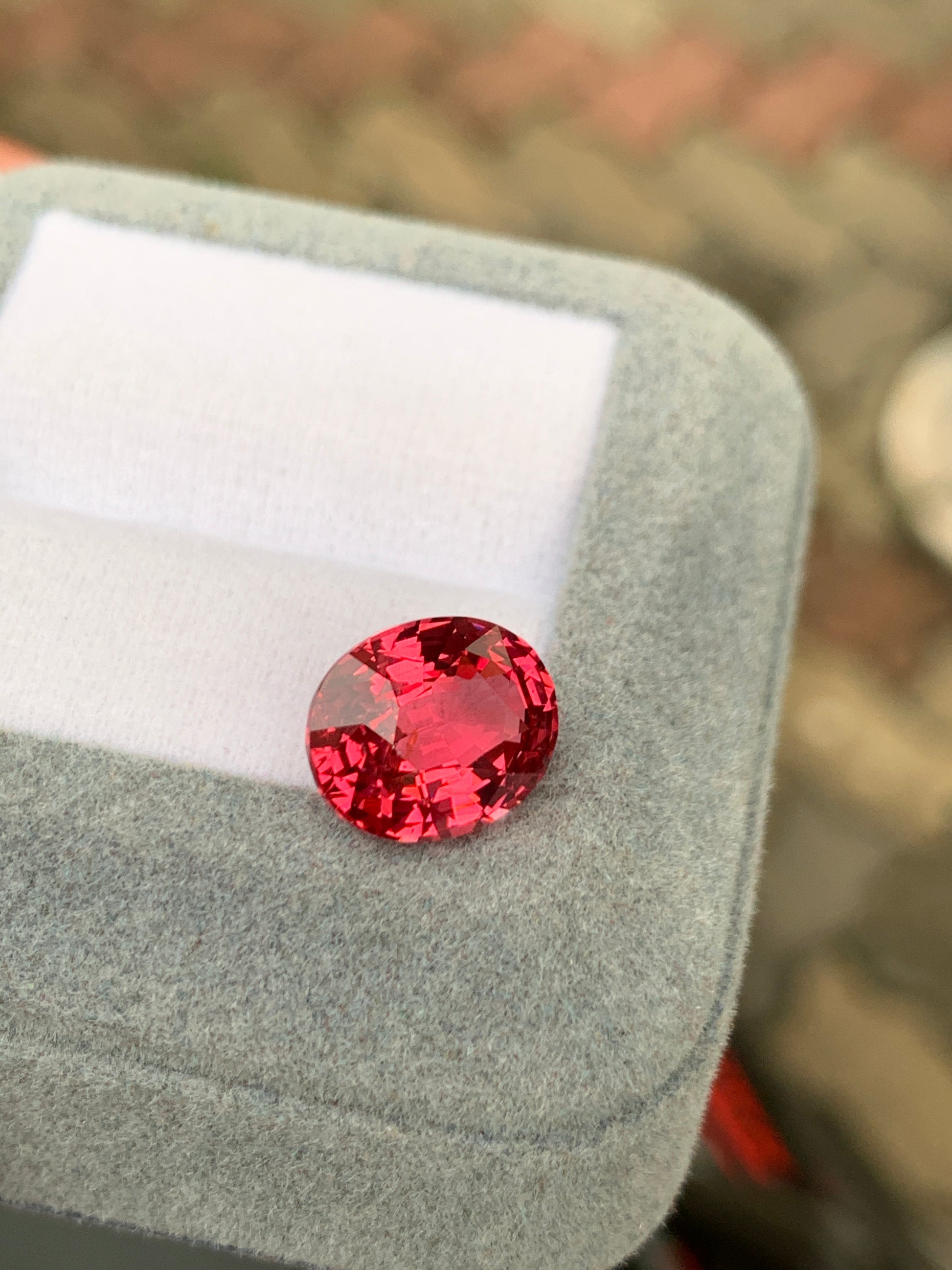 Un spinelle Mahenge rose vif de 5,00 carats, taille ovale, repose sur un écrin gris et blanc signé [NOUVEAU] Bonnot Paris. Le fond légèrement flou met en valeur la couleur vive et l'éclat de la pierre précieuse : une véritable pièce de haute joaillerie.