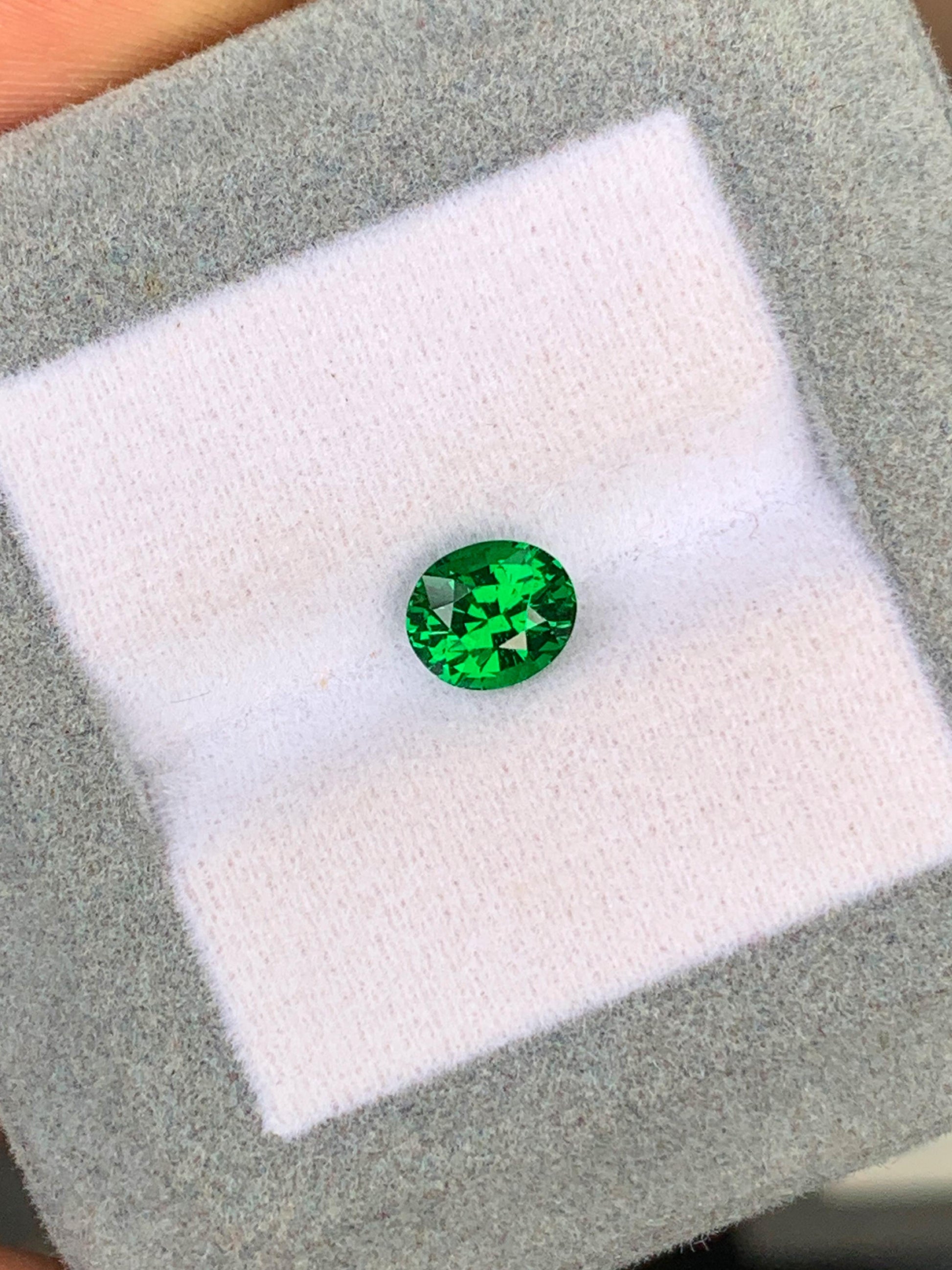 Une Tsavorite vibrante de 1,53 ct de [NOUVEAU] Bonnot Paris est présentée sur un fond coussiné blanc avec une bordure grise, ses facettes captant la lumière pour mettre en valeur sa clarté et sa couleur.